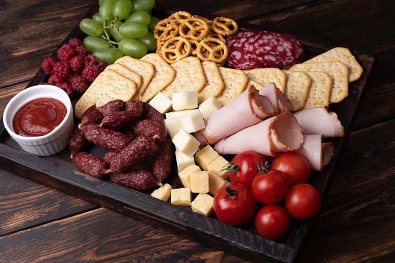 Sausage, cheese and fruit charcuterie board on a dark wooden background, party snacks, close-up.
