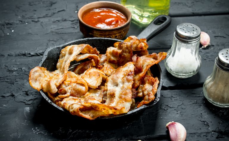 Fried bacon with tomato sauce. On black rustic background.