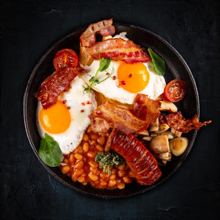 Flat lay of Full English Breakfast including sausages, grilled tomatoes and mushrooms, egg, bacon and baked beans