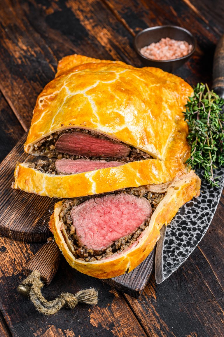 Homemade Beef Wellington puff pie with tenderloin meat on a cutting board. Dark wooden background. Top view.