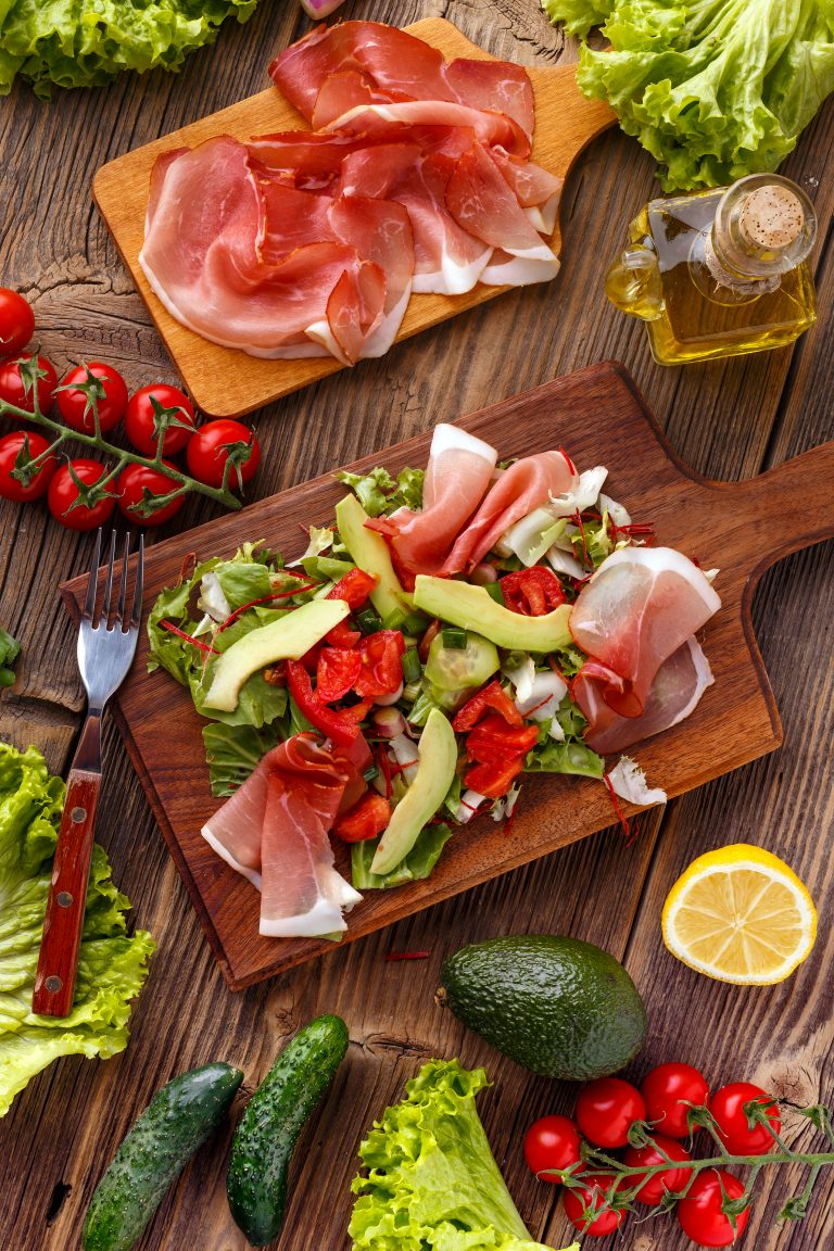 Mix of salad with smoked ham and vegetables on wooden cutting board
